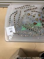 Clear plastic container of assorted costume jewelry including bracelets and rings laid flat with seller tag 46.