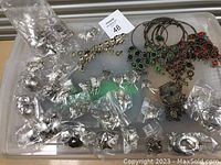 Photo of assorted silver-tone costume jewelry including earrings, bracelets, and pendants scattered and some bagged on a grey surface.