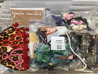 Overview of clear plastic bin containing assorted sewing ribbons, colorful feather packs, sewing fasteners and trims.