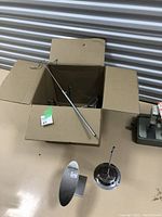 Chrome display stands including oval base with vertical rod, circular base with adjustable rod, and box with parts on a beige surface.