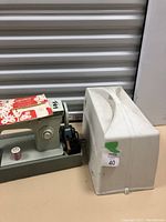 Photo of green and white Singer sewing machine with spool and foot pedal next to its hard carrying case