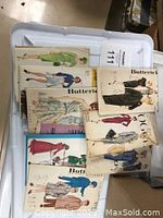 Box filled with vintage sewing patterns, featuring illustrated Butterick envelopes with mid-century women's dresses, suits, and costumes.