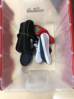 Multiple pairs of shoes including white runners, black Ugg boots, red embroidered shoes, and others placed in transparent bin.