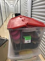 Clear storage bin with red lid containing multiple pairs of shoes in various colors and styles.