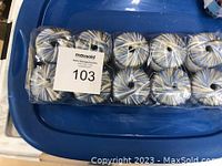 10 balls of variegated Elba yarn by Needful Yarns packaged in clear wrap on a blue tray.