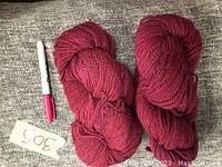 Two skeins of rose wool yarn laid on a textured surface with a pen beside for scale.