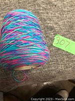 Close-up side view of multicolor yarn cone on a gray surface showing the variegated pattern.