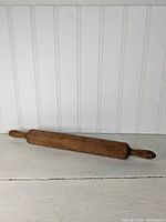 Full view of solid wood rolling pin resting horizontally showing overall length and handles.