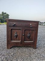 Front view of antique wooden wash stand showing grape cluster carvings on cabinet doors and drawer above.