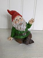 Acrylic gnome figurine shown seated with red pointed hat, green jacket, white beard and brown pants.