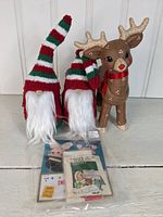 Two handmade gnomes with red, green, and white striped hats, a handpainted brown reindeer figurine with a red ribbon collar, and a bag of vintage Christmas tags with various designs.