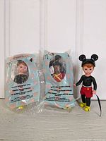 Photo shows two Madame Alexander Mickey Mouse dolls in original sealed McDonald Happy Meal packaging and one unboxed Madame Alexander Mickey Mouse doll wearing black mouse ears, yellow shoes, red shorts, and black top.