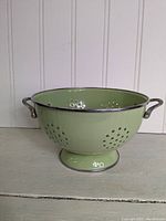 Front side view of large green enamel metal colander with perforations and handles.