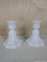 Two low milk glass candle stick holders on a wooden surface, showing shape and finish