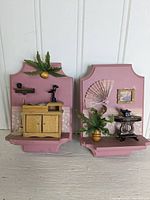 Two small pink wall plates each with miniature room furniture displays shown against a white paneled background.