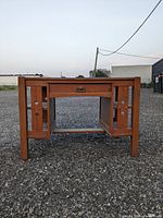 Front view of oak desk showing the drawer and side panel design with circular cut-out accents.
