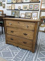 Frontal view of oak dresser with three drawers; top drawer has glass knobs, bottom drawers have metal handles; dresser wood grain visible, no top panel underneath.