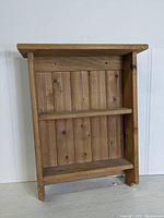 Front view of unfinished pine wall shelf with two shelves and vertical back paneling.