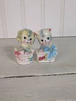 Front view of two ceramic puppy salt and pepper shakers, showing detailed puppy faces and basket designs.