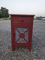 Front view of a small red wooden cabinet showing one drawer and mirrored door with cross braces.