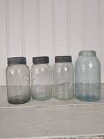 Photo showing set of four vintage Crown glass jars on a white shelf, three clear and one large blue jar with metal lids.