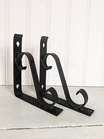 Pair of black cast iron shelf brackets shown from an angle displaying the two brackets together.