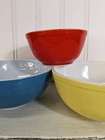 Three Pyrex bowls stacked and arranged to show colors and sizes: red, blue, and yellow bowls.