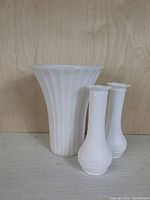 Three white milk glass vases of varying sizes, fluted vertical pattern visible