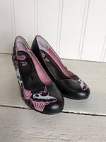 Front and side angle view of black T.U.K. high heels with pink and white cupcake and skull designs.