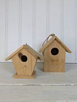 Two wooden birdhouses, one shorter around 6 inches with side door access, one taller about 8 inches with front circular hole entrance.