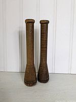 Photo showing two tall vintage wooden spools standing upright against a plain light background. Both spools have textured, grooved wood with dark natural patina and flat tops.