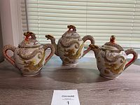 Front view of three piece tea set on table with teapot, sugar and cream containers decorated with gold and red dragons.