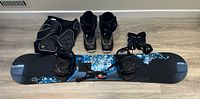 Snowboard gear including Burton board with Flow bindings, Burton boots, Dakine wrist guards, and R20 pants laid out on floor