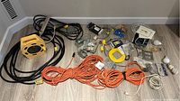 Overview photo showing all electrical items on the floor including extension cords, power reel, wire nuts, electrical boxes, and other electrical accessories.