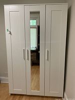 Front view of white IKEA wardrobe with three doors, middle door featuring a mirror