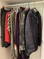 Wardrobe shot showing a variety of women's clothing items hung on hangers including jackets, skirts, and tops in various colors such as black, grey, red, purple, and patterned.