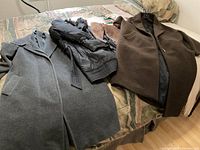 Overhead view of all four coats laid out on a bed: grey wool coat, black puffer coat with scarf, brown Zara coat, brown leather jacket