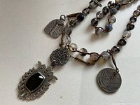 Close-up of black gemstone pendant and silver-tone decorative charms on bead strand.