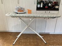Full view of ironing board with iron and cover showing green leaf pattern on ironing board.