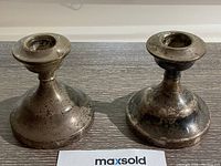 Front view showing the pair of small, tarnished sterling silver candlesticks with wide bases on a wood surface.