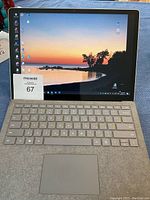 Open Surface Pro showing attached Type Cover keyboard and powered-on display with scenic wallpaper, sticker #67 visible