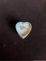 Gold ring displayed inside a colorful heart-shaped box with cushioned white interior, showing the overall presentation and condition of the ring and box.