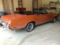Rear three-quarter view of bronze metallic body with black convertible top down in garage