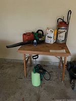 Full lot showing blower, oil, herbicide, sprayers on top of wooden folding table