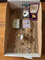 Full assortment of costume jewelry including necklaces, rings, earrings, brooches, and a miniature frame arranged in cardboard tray