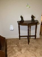Demi lune table with metal fish bookends on top, showing front view in a room with beige carpet.