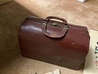 Closed vintage brown leather doctor's bag with top handle on carpeted floor