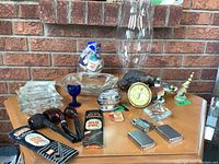 Top view of table with pipes, lighters, ashtrays, decorative ceramic birds, hygrometer, magnifying glass, blue glass goblet and glass hurricane lamp shade.