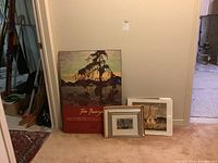 Photo of the large Tom Thomson poster, three framed prints leaning against the wall on carpet, one smaller print and informational sheet visible