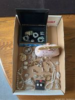 Overview of assorted rhinestone jewellery pieces arranged in a box and around it, including bracelets, brooches, earrings, and necklaces.